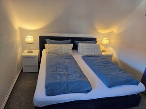 Un lit double avec deux oreillers, une table de chevet avec une lampe et une petite table de nuit avec une lampe.