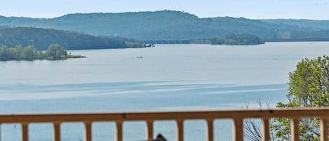 A view from a balcony overlooking a large body of water with a forested hill in the background.