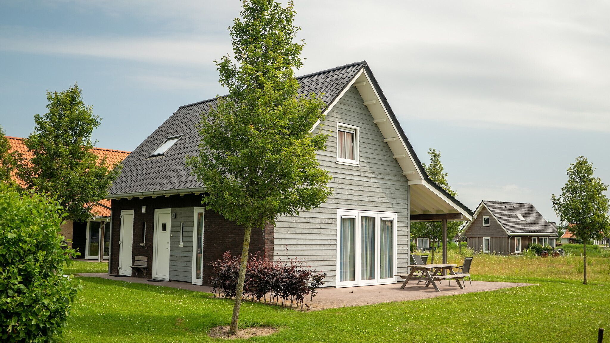 Een modern huis met twee verdiepingen, een schuin dak, een overdekt terras en een verzorgd gazon.