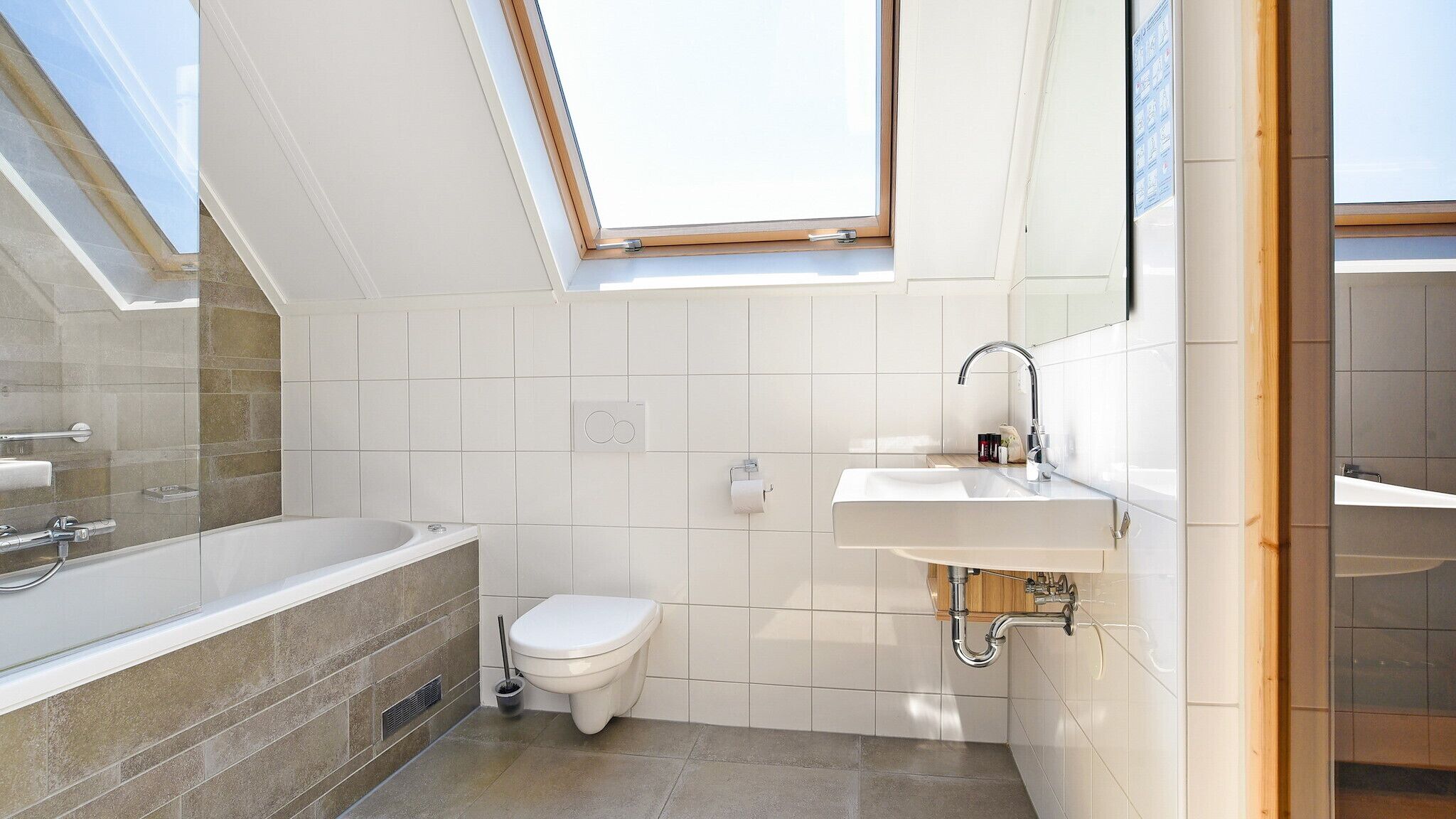 A modern bathroom with a skylight, a bathtub, a toilet, and a sink.