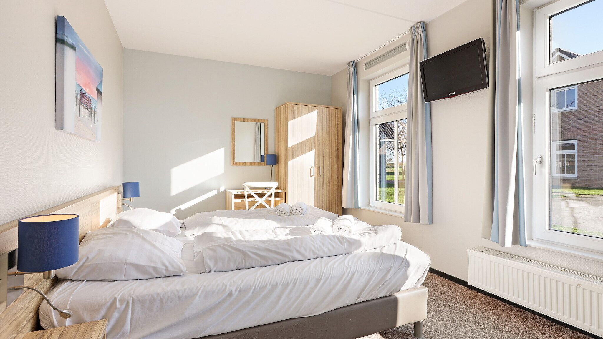 A bedroom with a bed, a desk, a chair, a mirror, and a TV.