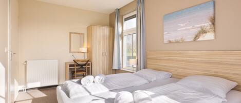Ein Hotelzimmer mit Bett, Schreibtisch, Stuhl, Heizkörper, einem Fenster mit Vorhängen und einem Bild an der Wand.