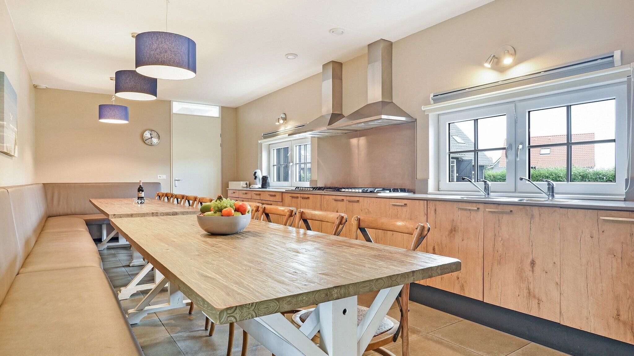 A modern kitchen with a wooden dining table, a bowl of fruit, and a large window.