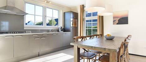 Eine moderne Küche mit Edelstahlgeräten, einem großen Fenster und einer Essecke mit Holztischen und -stühlen.