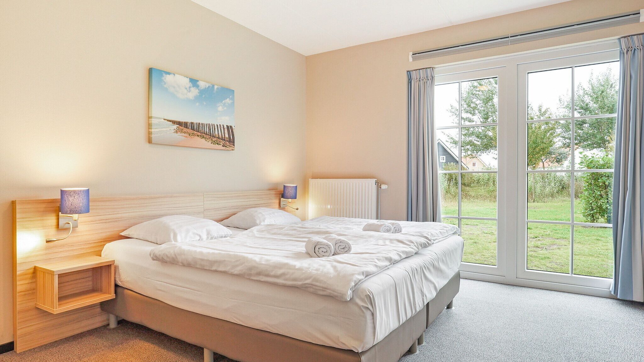 Una camera d'albergo con un letto grande, due comodini con lampade, un quadro appeso al muro e una vista attraverso un'ampia finestra.