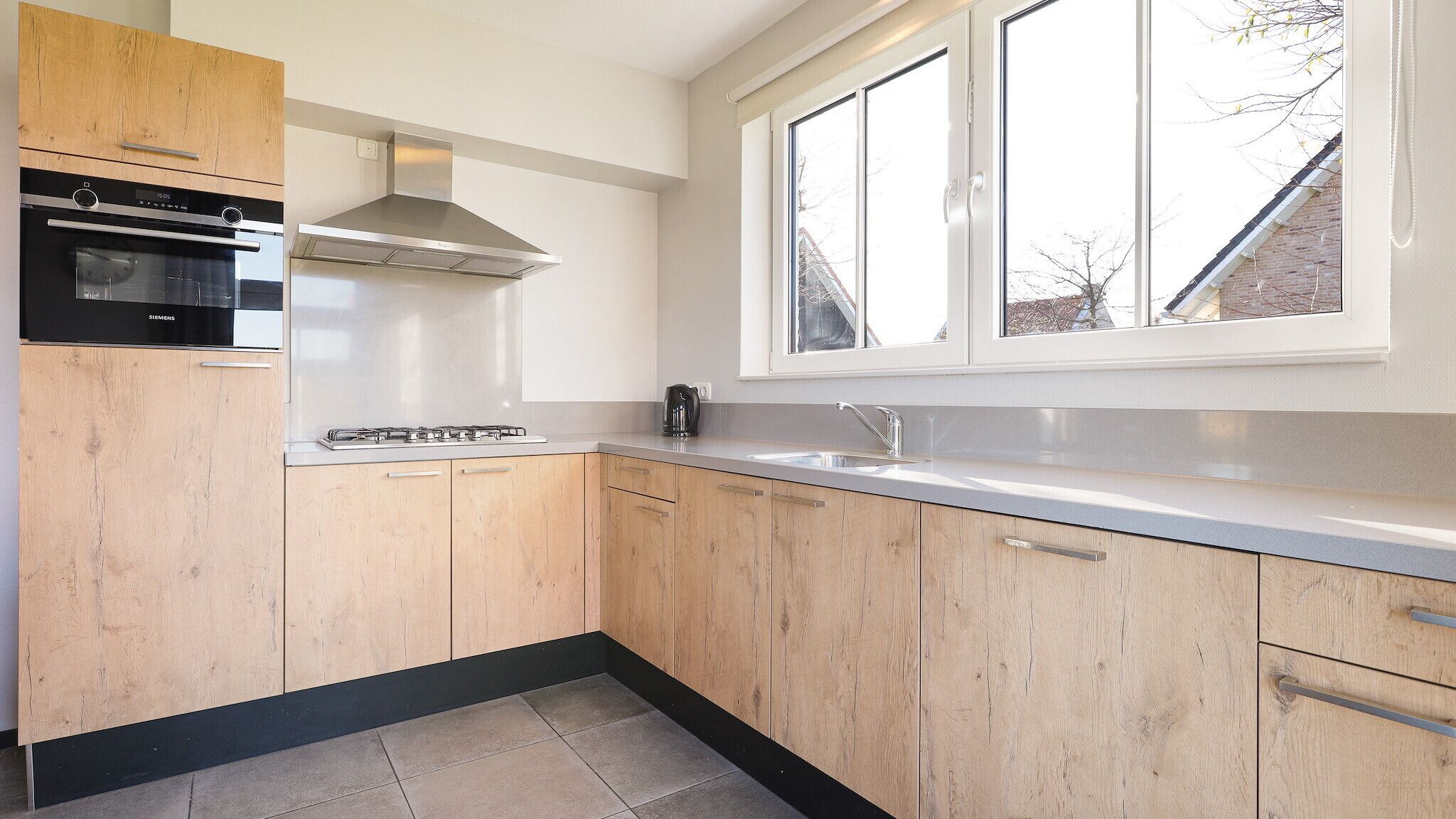 Une cuisine moderne avec des meubles en bois, un four encastré, une cuisinière à gaz et une fenêtre au-dessus de l’évier.
