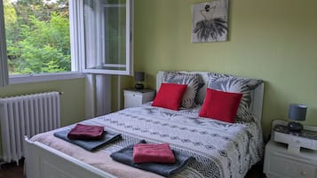 A bedroom with a bed, two nightstands, a window, a radiator, and a painting on the wall.