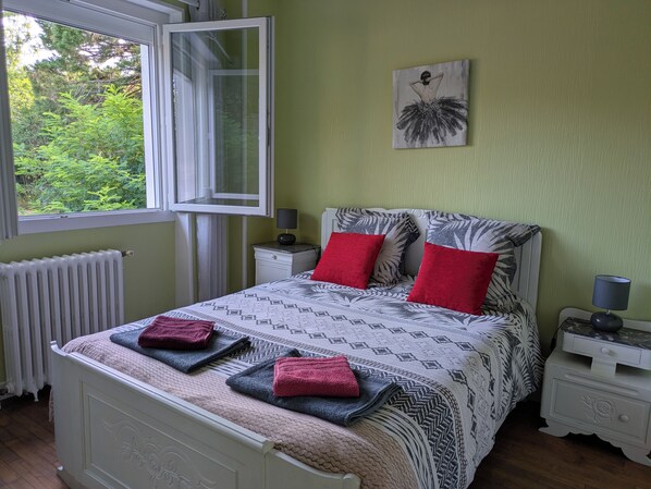 Ein Schlafzimmer mit einem Bett, zwei Nachttischen, einem Fenster, einer Heizung und einem Bild an der Wand.