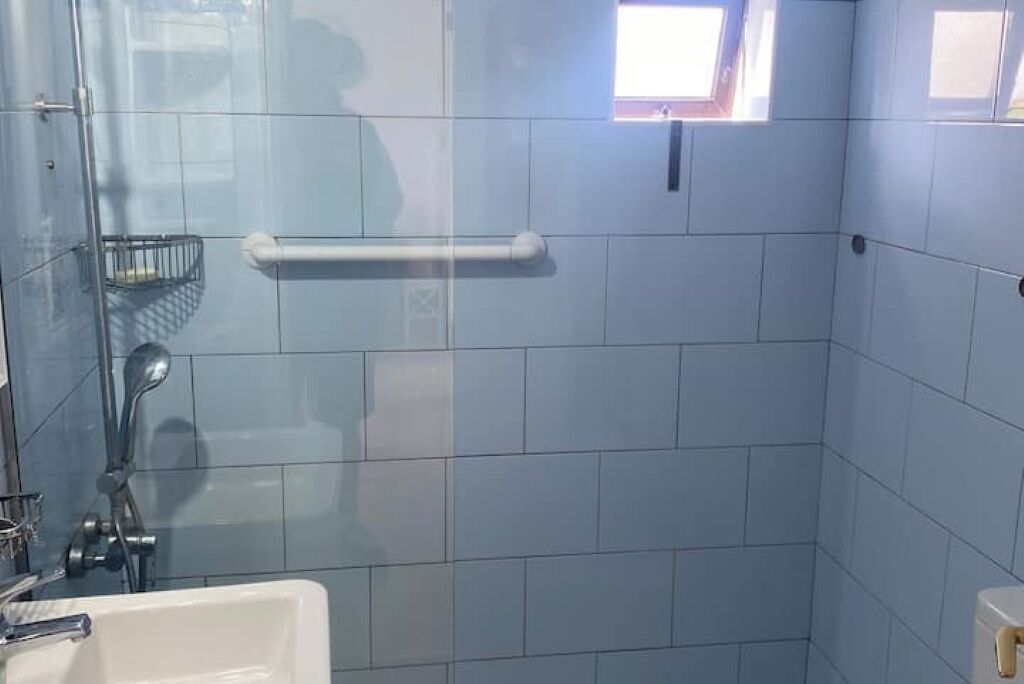 A bathroom with a glass shower enclosure, a white sink, and a small window.