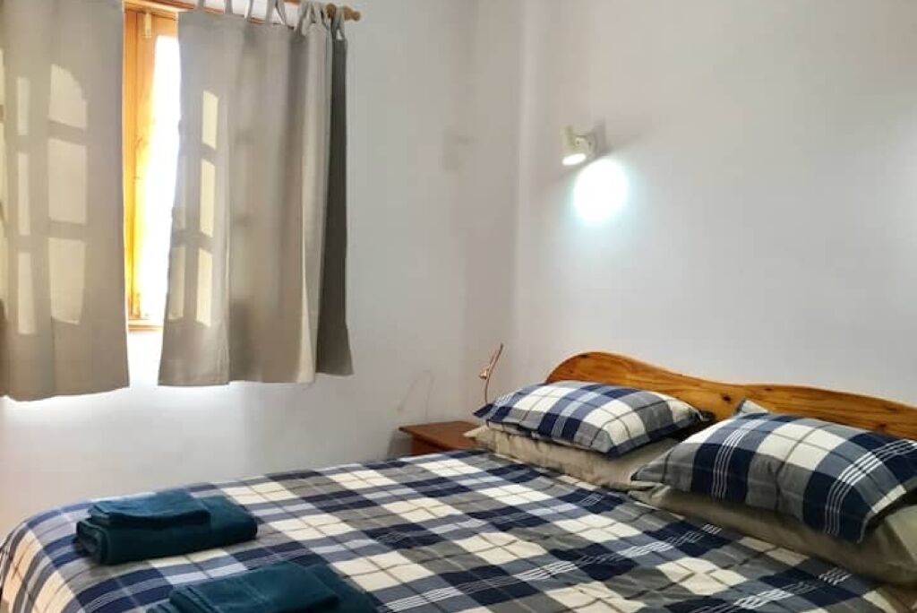 A bedroom with a bed, curtains, a nightstand, and a wall-mounted light.