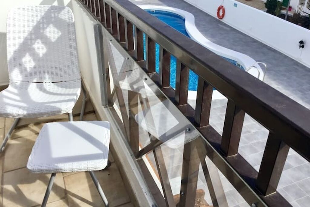 A balcony with a pool, white chairs, and a safety railing.