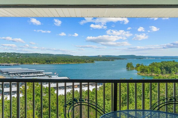 A balcony with a view of a lake, surrounded by greenery and buildings.