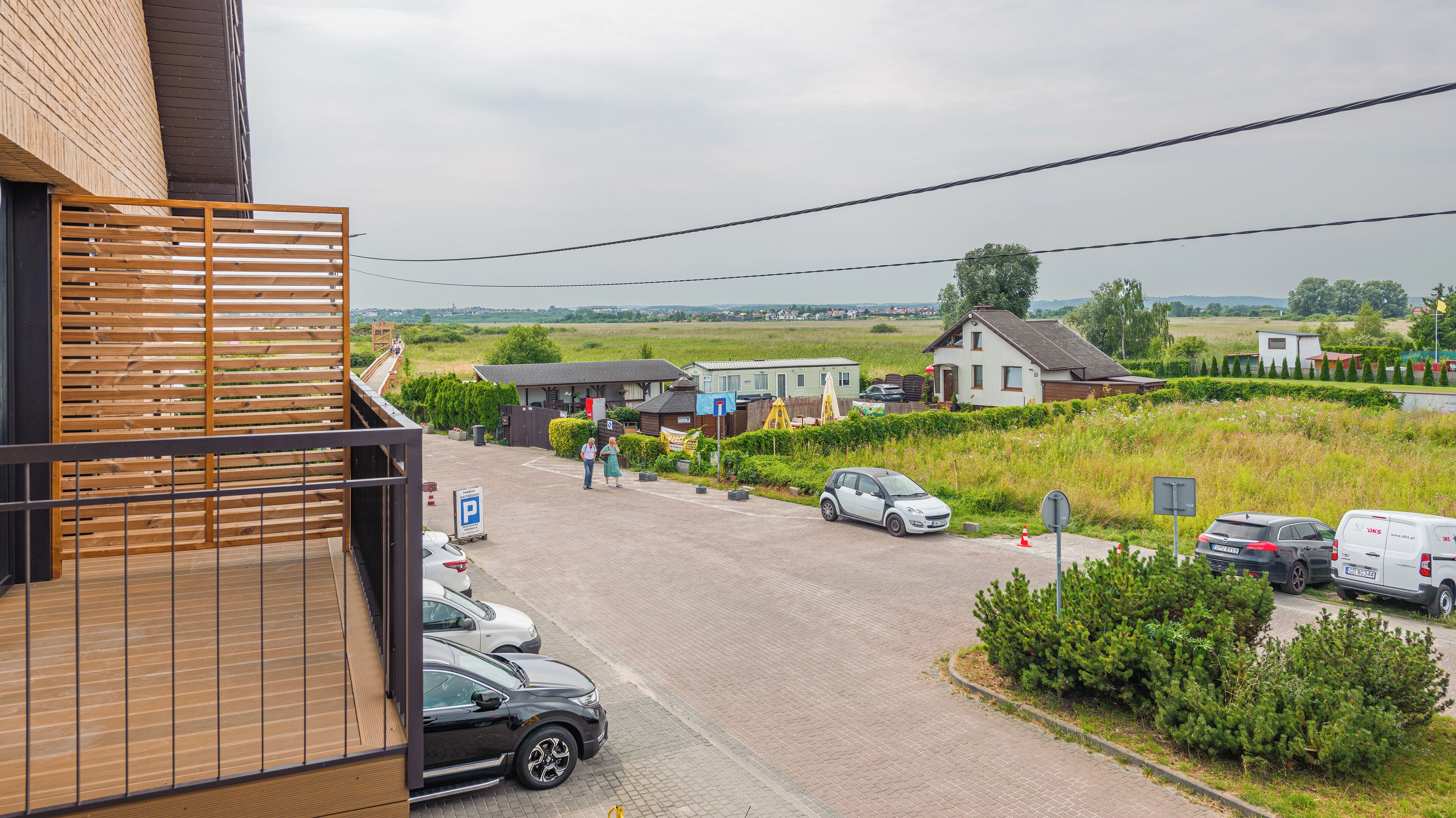 A residential area with houses, a parking lot, and a wooden balcony overlooking the street.