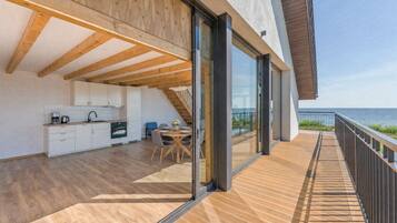 A modern kitchen with wooden beams, a dining area with a table and chairs, and a balcony with a view of the sea.