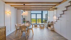 A dining area with a table set for four, a sofa, and a view of the outdoors. - Apartamenty Sun & Snow Bursztynowa Rewa (Kosakowo)