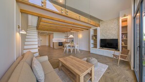 A spacious living area with a wooden staircase, a dining table, and a TV mounted on a stone wall. - Apartamenty Sun & Snow Bursztynowa Rewa (Kosakowo)