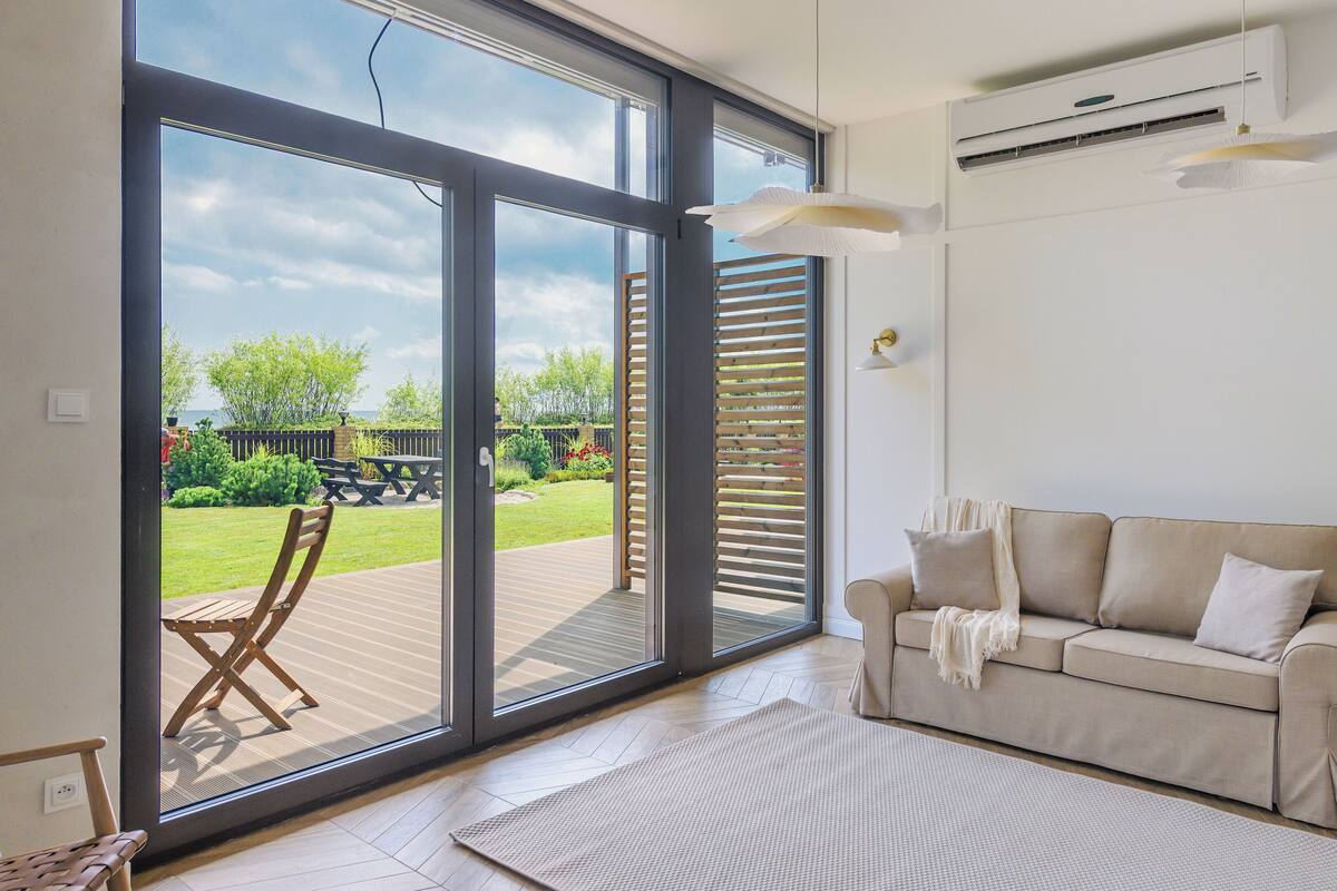 Ein modernes Wohnzimmer mit einer Schiebeglasdoor zum Patio, einem beigefarbenen Sofa und einem großen Fenster mit Jalousien.