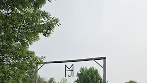 Ein unbefestigter Weg führt zu einem verschlossenen Eingang mit einem hölzernen Tor und je einer amerikanischen Flagge auf jeder Seite.