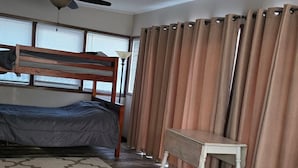 Ein Zimmer mit Etagenbett, Schreibtisch, Deckenventilator und einem Fenster mit Jalousien.