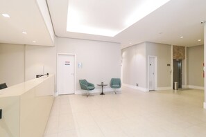 A modern hotel lobby with a reception desk, two green chairs, a small table, and an elevator. - ADD Nova Berrini (Sao Paulo)