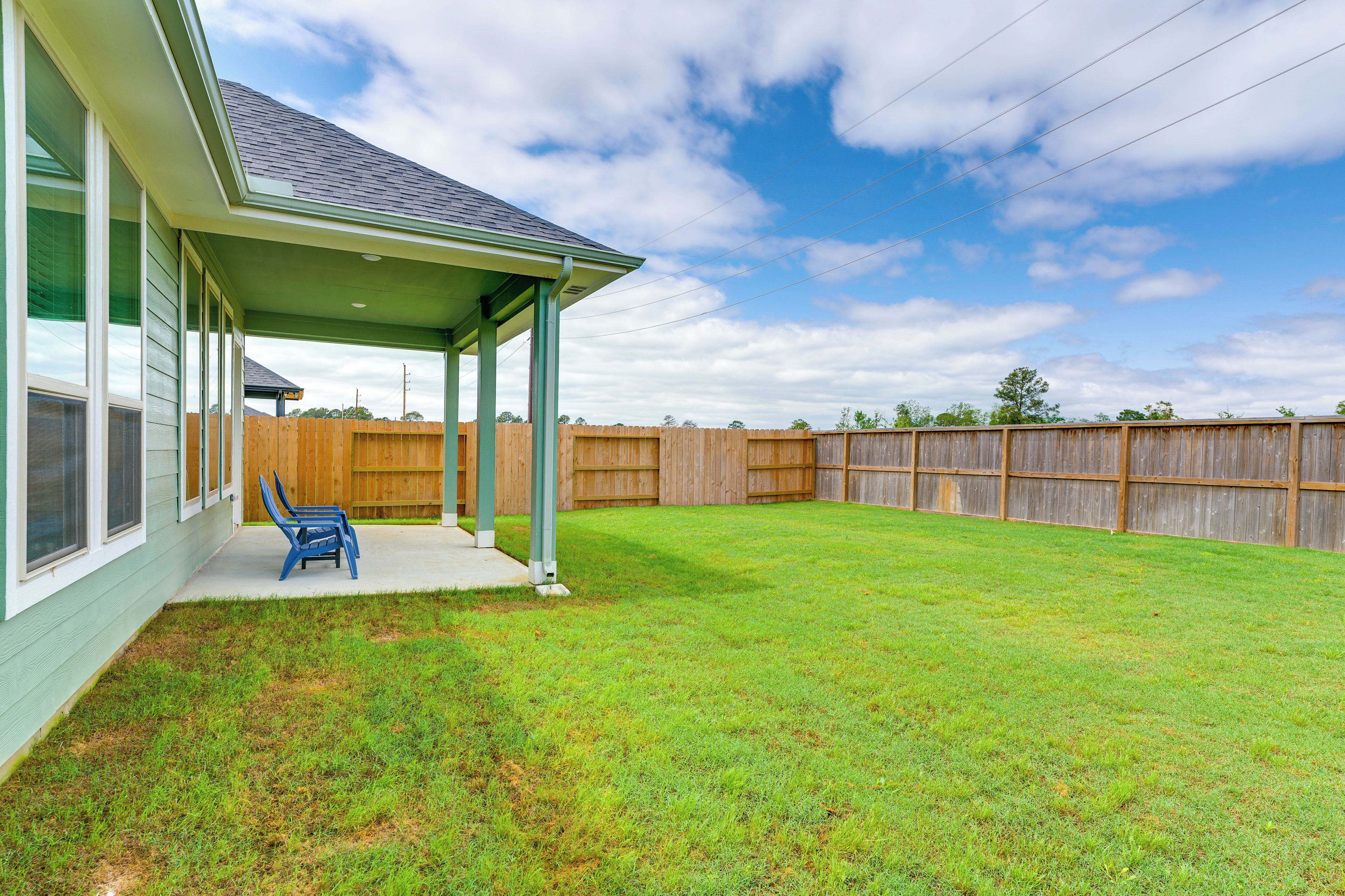A backyard with a covered patio, a wooden fence, and a grassy lawn.