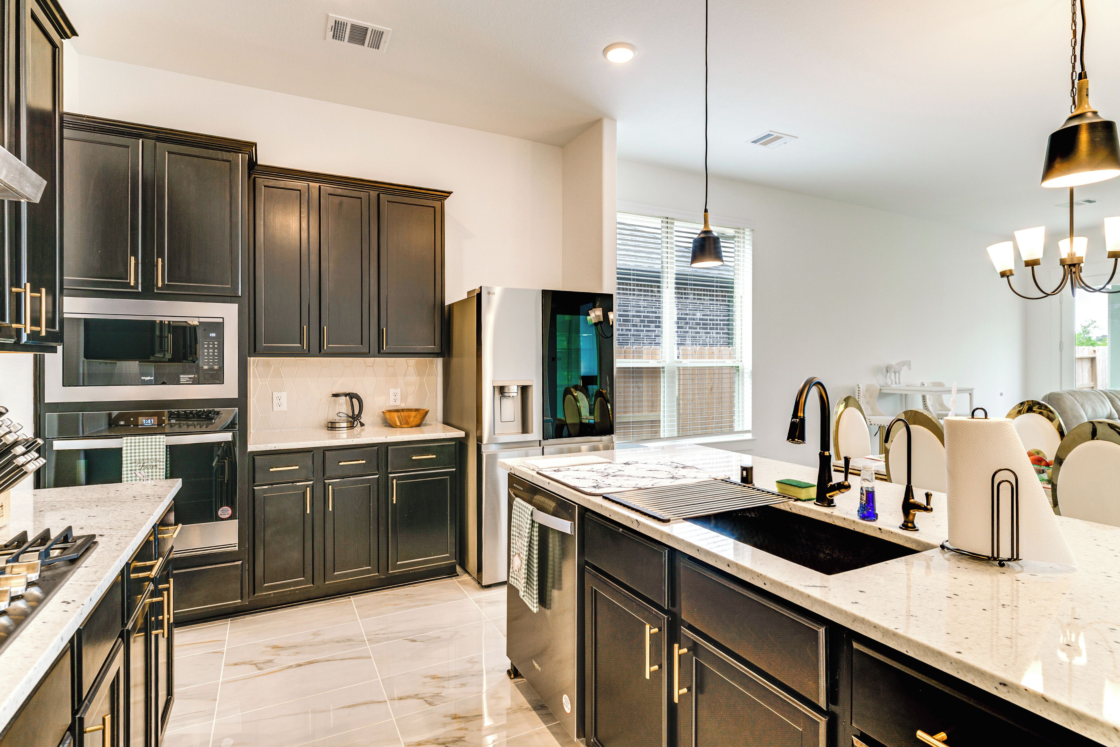 A modern kitchen with dark cabinets, stainless steel appliances, a large island with a sink, and pendant lighting.