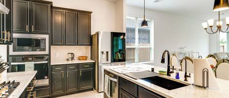 A modern kitchen with dark cabinets, stainless steel appliances, a large island with a sink, and pendant lighting.