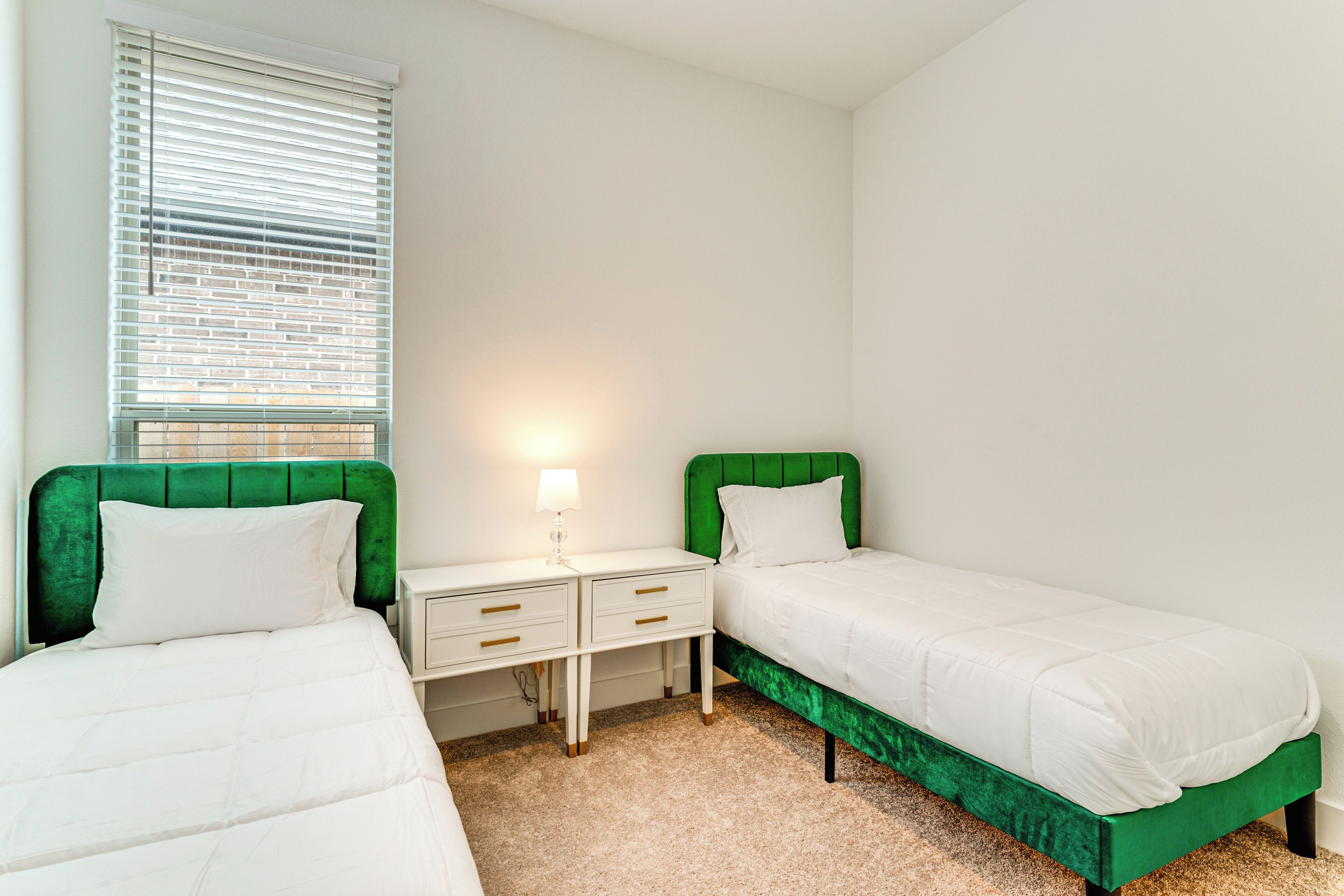 Een slaapkamer met twee bedden, een nachtkastje en een raam met zonwering.