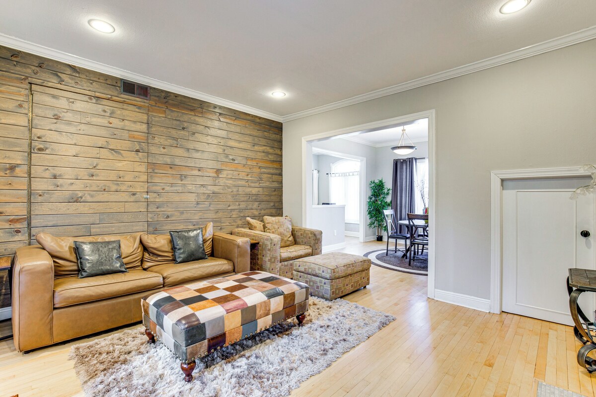 A living room with a wooden wall, a brown leather sofa, a patterned ottoman, and a fluffy rug.