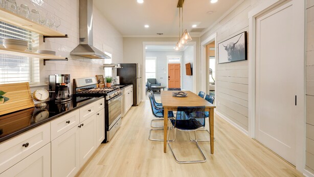 A modern kitchen with a central island, wooden cabinets, and a dining area with blue chairs. - San Antonio Home 2 Mi to Dtwn, Swim Spa! (San Antonio)