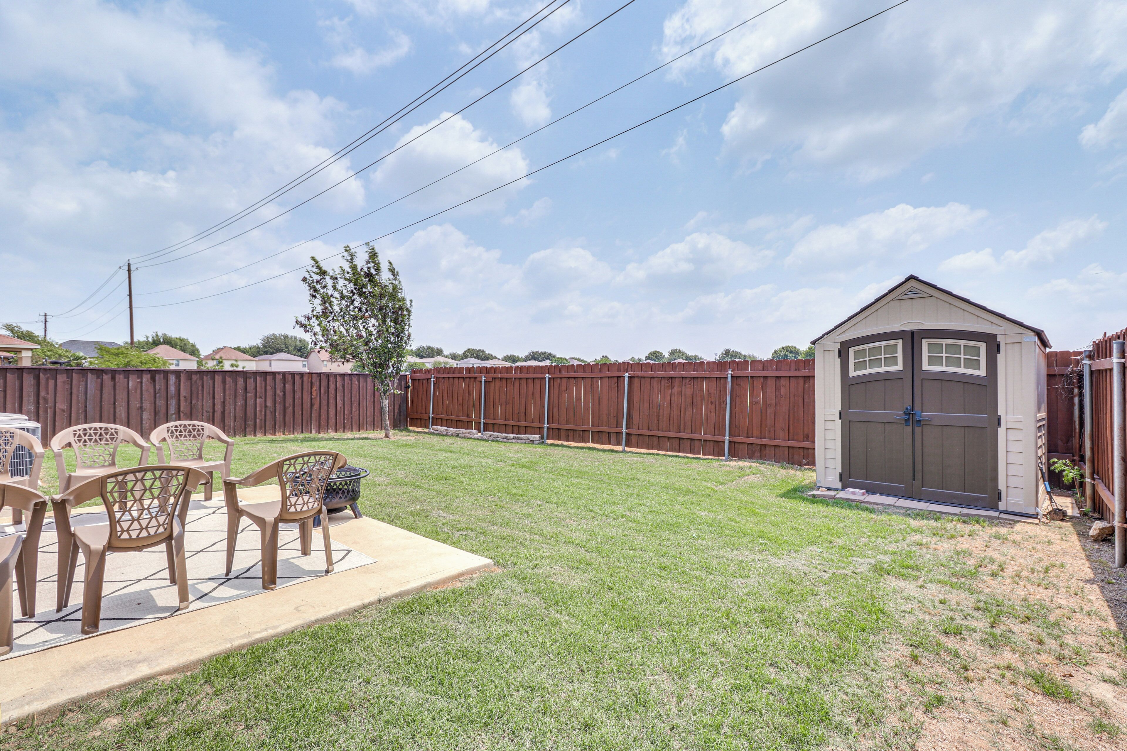 A backyard with a patio, chairs, a shed, and a wooden fence.