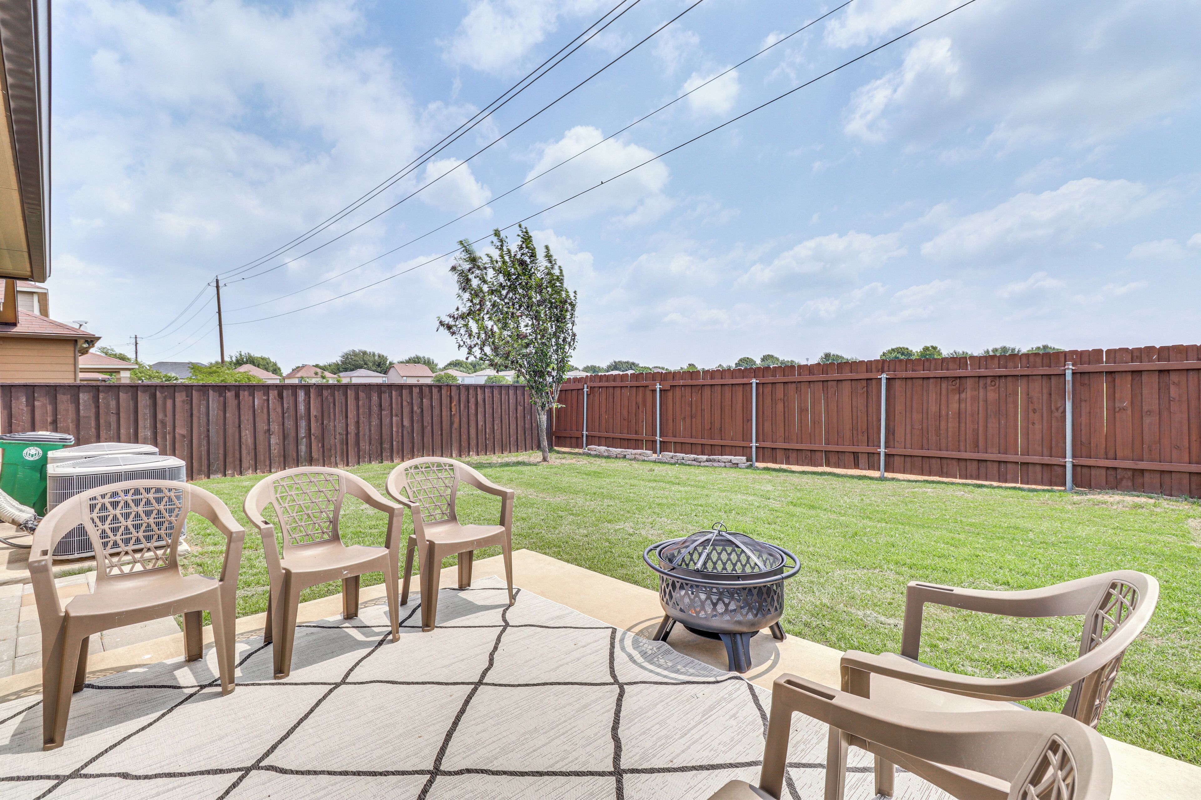 A patio with outdoor furniture, a fire pit, and a view of a backyard with a wooden fence.