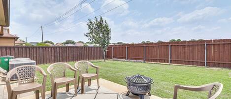A patio with outdoor furniture, a fire pit, and a view of a backyard with a wooden fence.