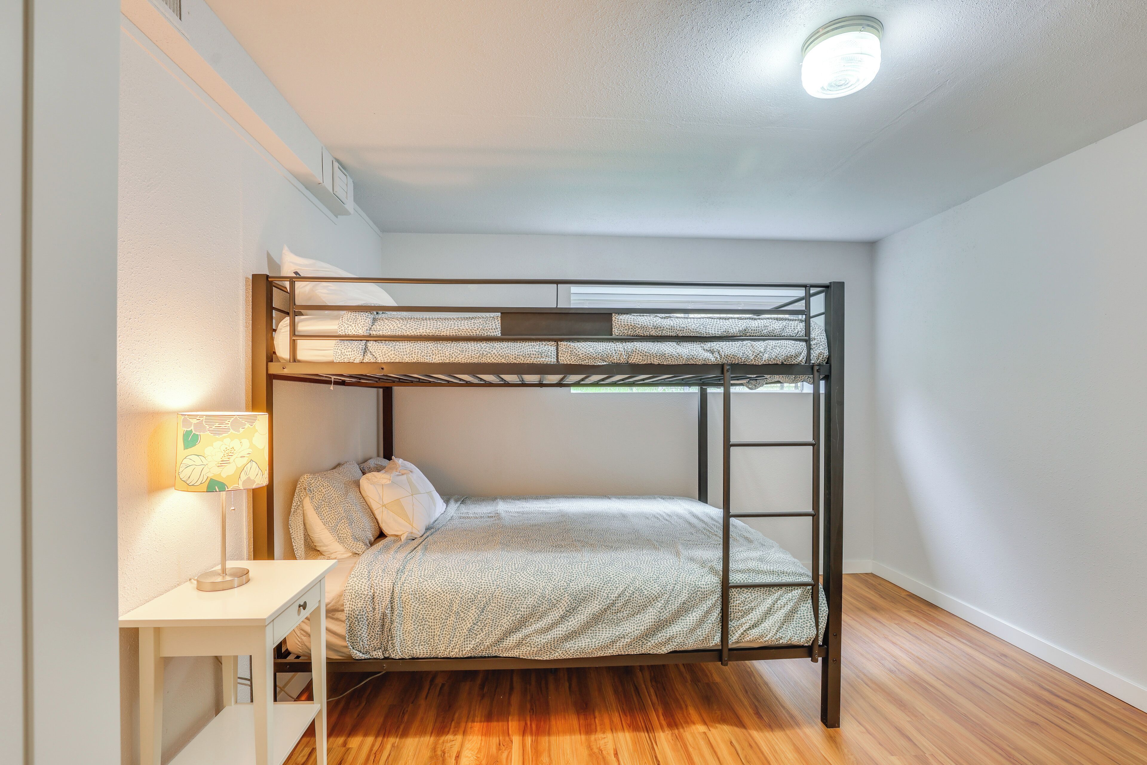 A bunk bed with a desk and lamp, wooden flooring, and a ceiling light.