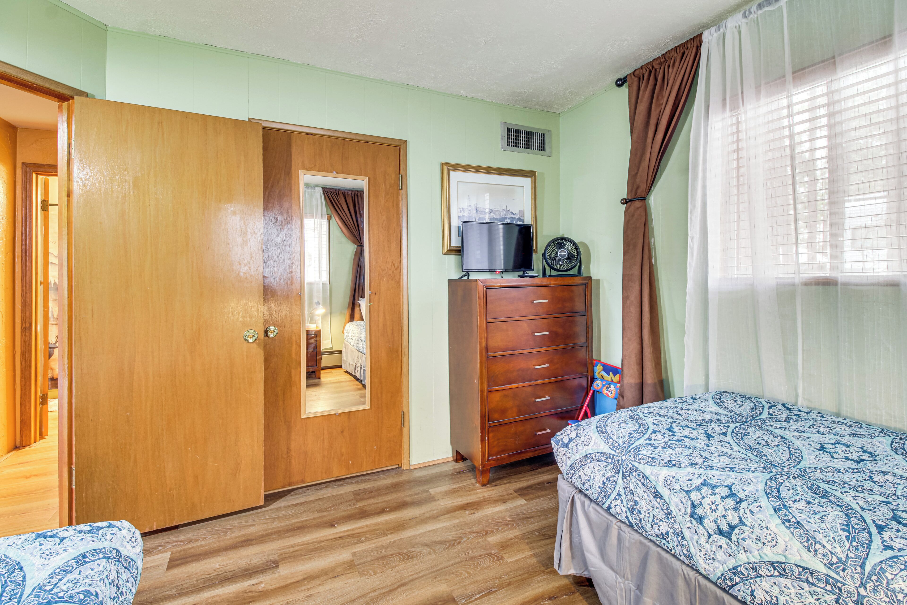 Une chambre à coucher avec une armoire en bois, un lit avec une literie à motifs, une commode, un miroir et une fenêtre avec des rideaux.