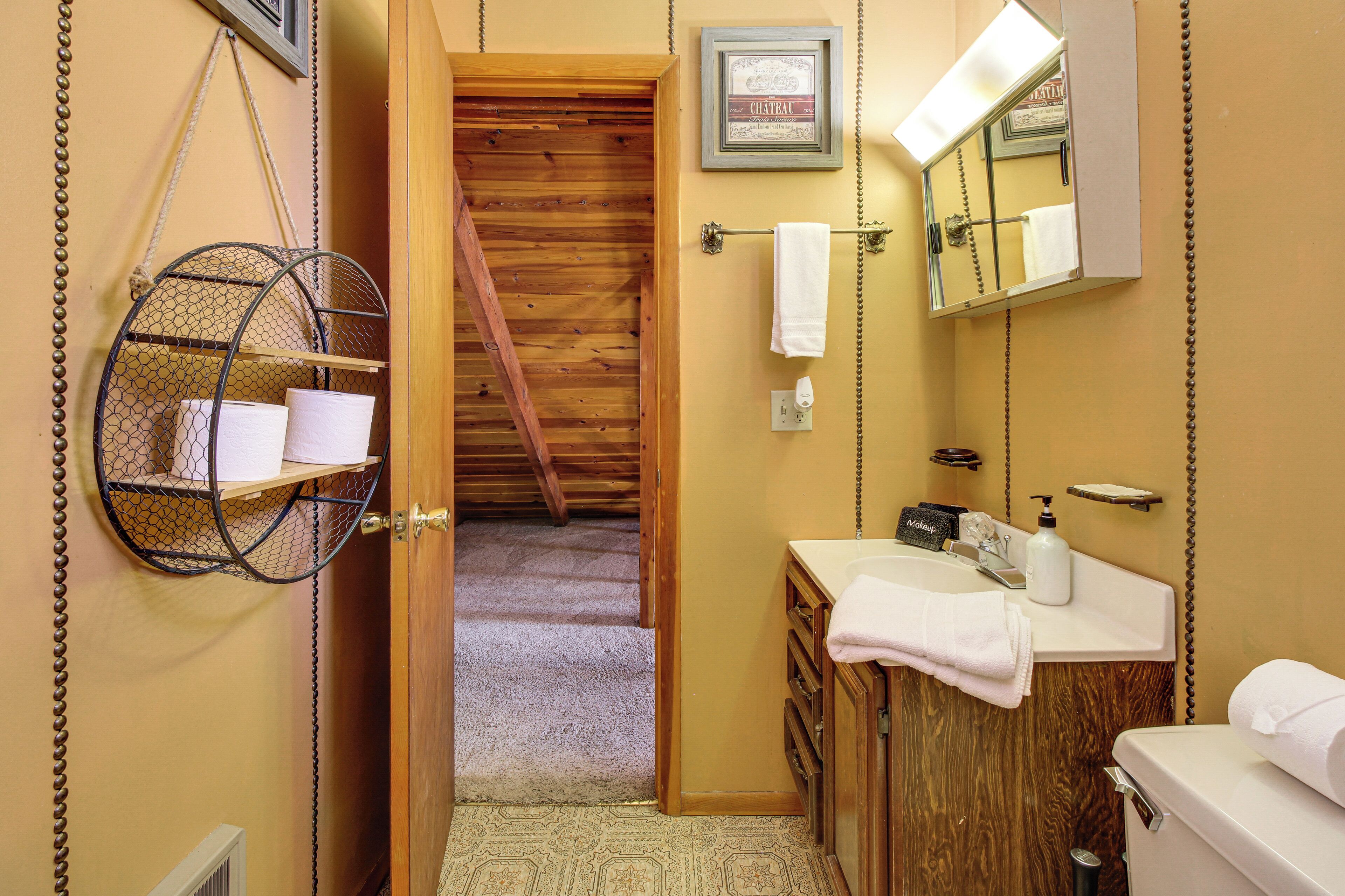 A bathroom with a wooden door, a hanging towel rack, a sink with a mirror, and a framed picture on the wall.