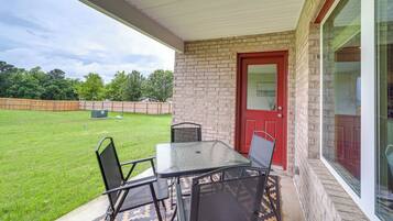 A covered patio with a table and chairs, a red door, and a view of a grassy yard.