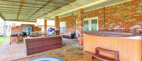 Un patio techado con pared de ladrillo, un jacuzzi, una parrilla y una zona de estar.