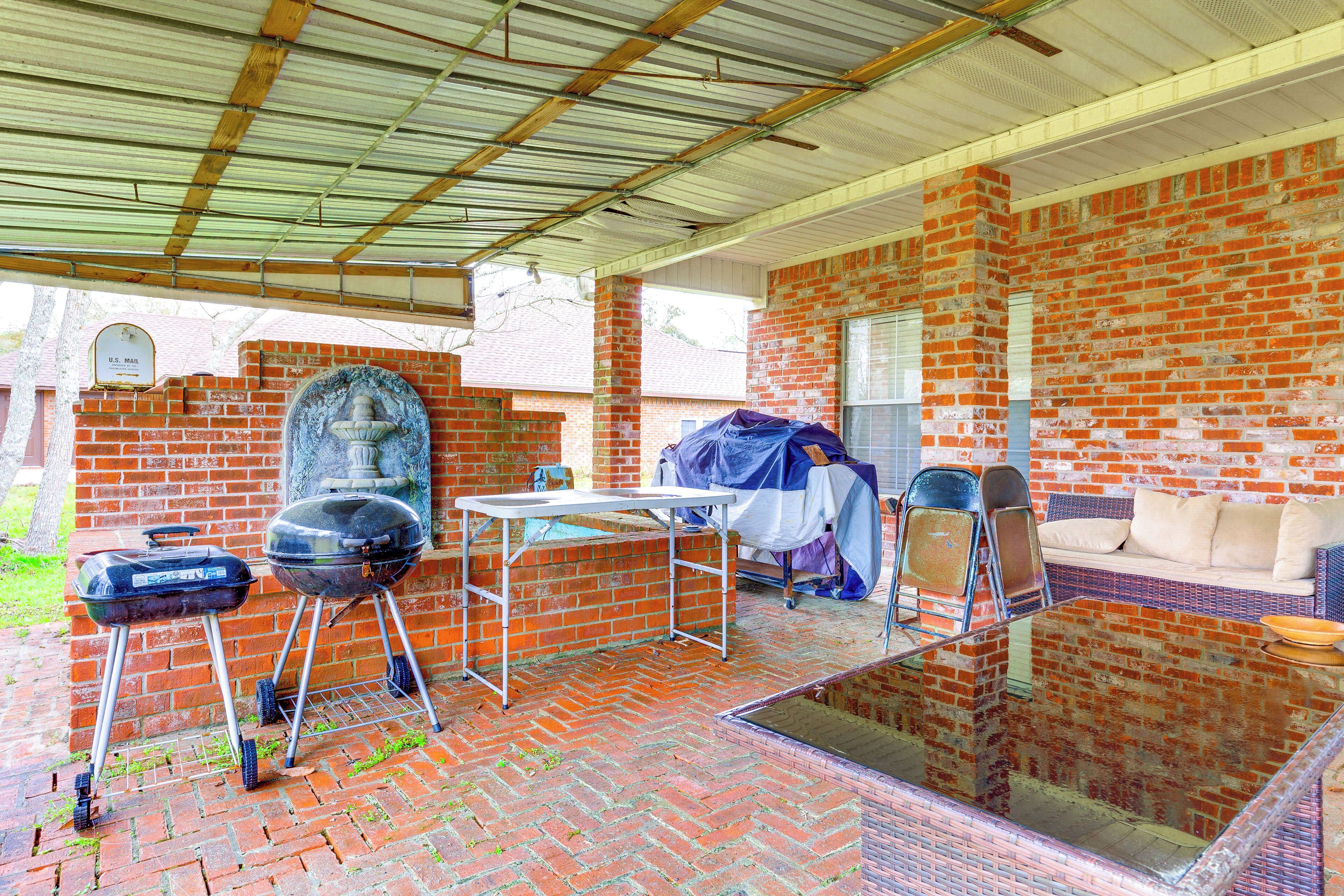Un patio al aire libre con pared de ladrillo, zona cubierta con mesa y sillas, y una parrilla.