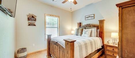 A bedroom with a wooden bed, a nightstand, a lamp, a ceiling fan, and a window with blinds.