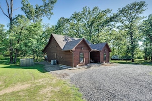 A rustic cabin with a gravel driveway and a covered outdoor seating area, surrounded by trees.