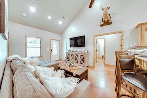 A spacious living room with a large sofa, a wooden dining table, and a mounted television.