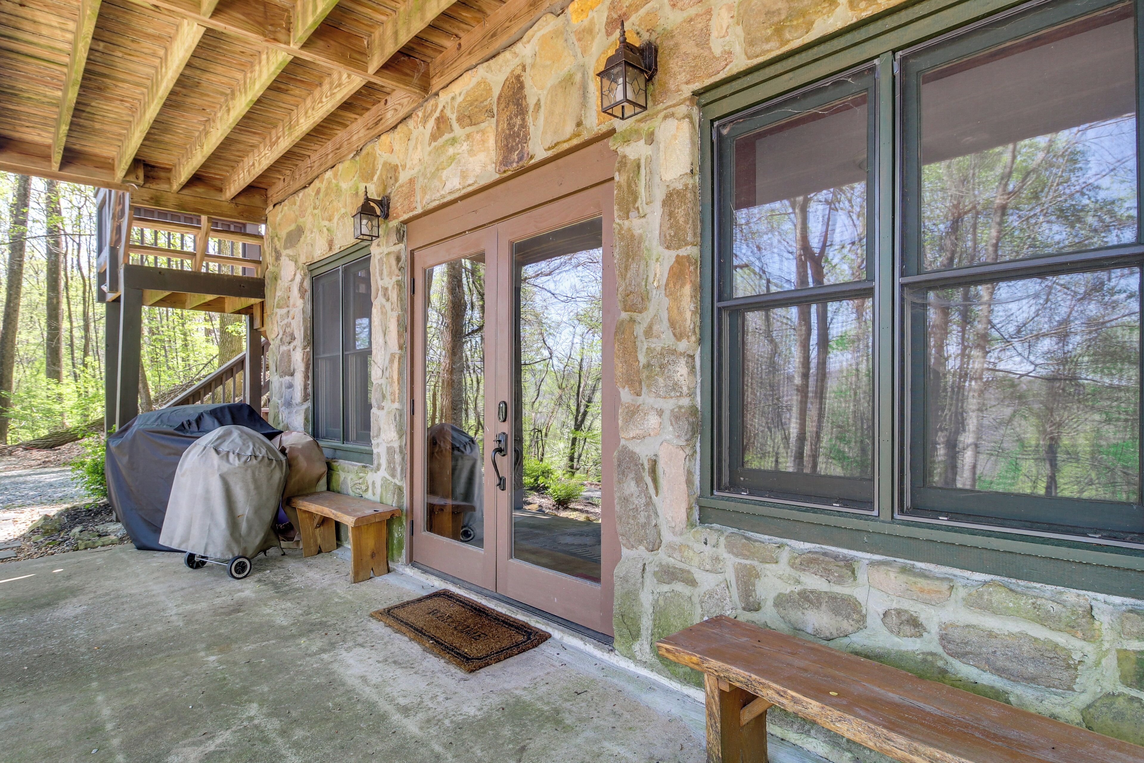 Ein Steinhaus mit überdachter Veranda, einer Bank und einem überdachten Grill.