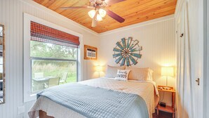 A bedroom with a bed, a ceiling fan, a window with blinds, a wall clock, and a bedside table with a lamp. - 8 Mi to Dtwn Wimberley: Cabin Retreat on 5 Acres! (San Marcos)