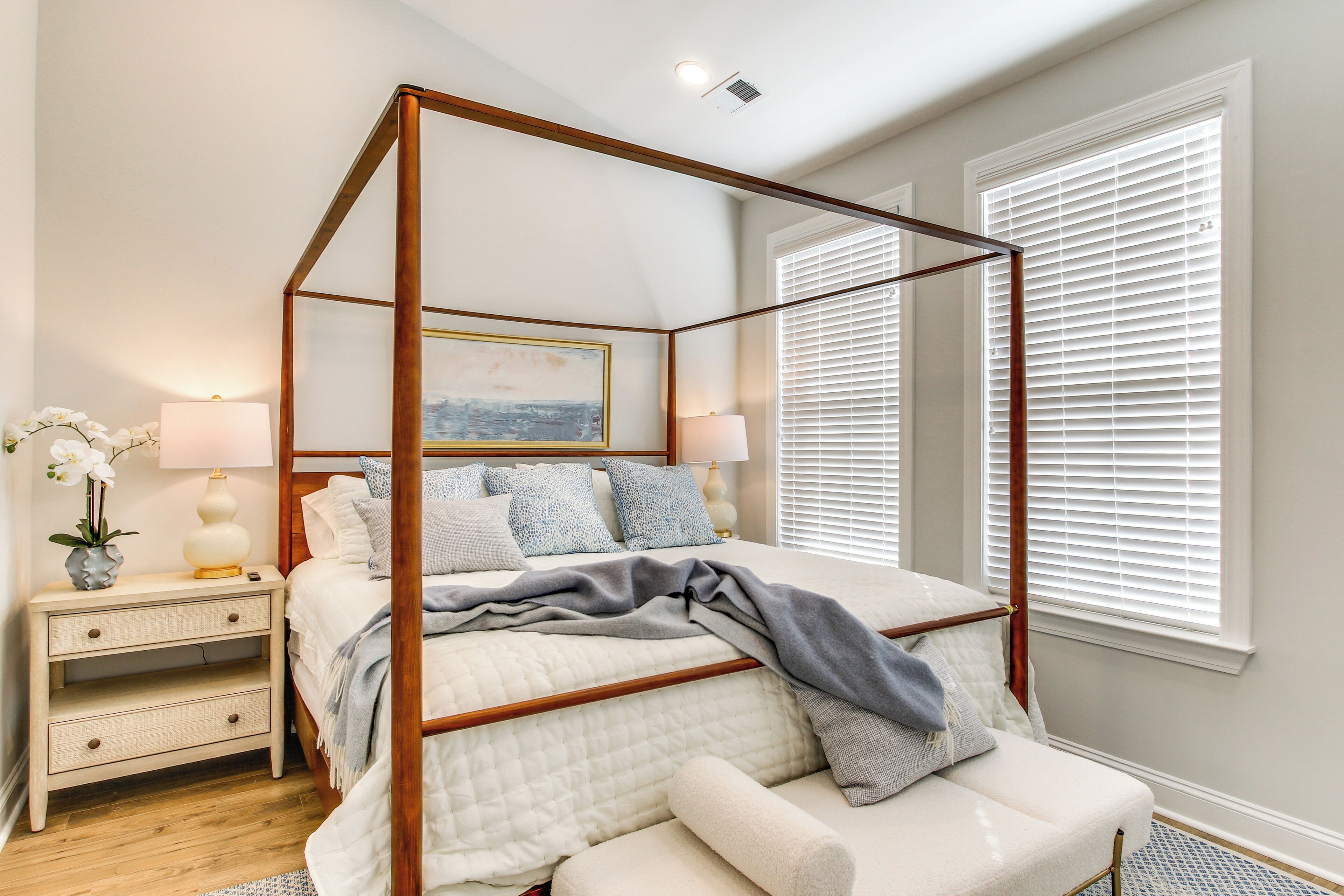 A four-poster bed with a wooden frame, a bedside table with a lamp, and a window with blinds.