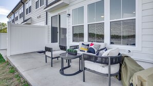 Ein überdachter Patio-Bereich mit Außenmöbeln, großen Fenstern und einer weißen Fassade.