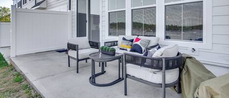 Ein überdachter Patio-Bereich mit Außenmöbeln, großen Fenstern und einer weißen Fassade.