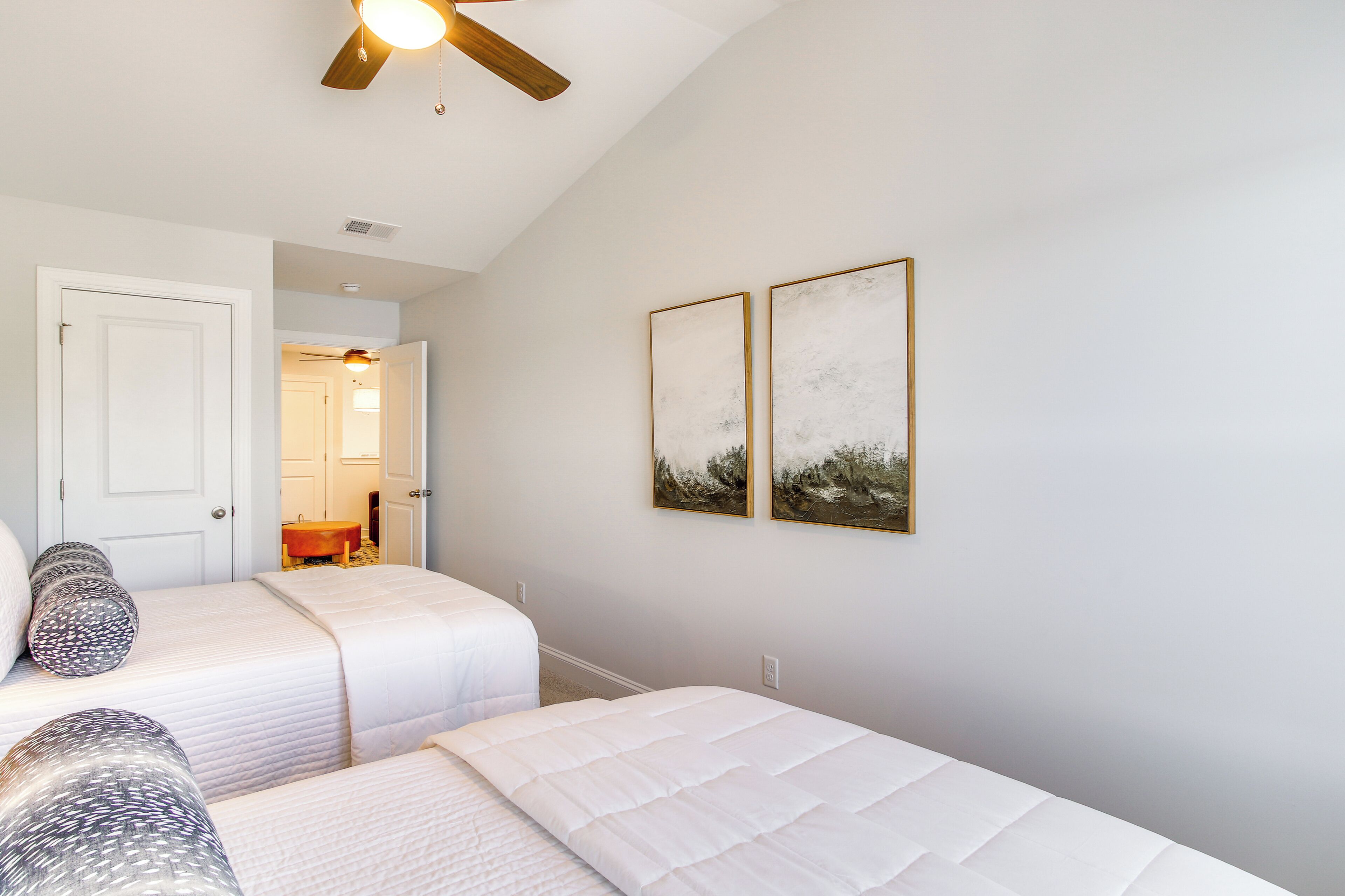 A bedroom with two beds, a ceiling fan, and artwork on the wall.