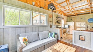 A cozy cabin interior with a sofa, wooden beams, a kitchen area, and large windows. - Secluded on 10 Acres: Livingston Getaway w/ Sauna! (Livingston)