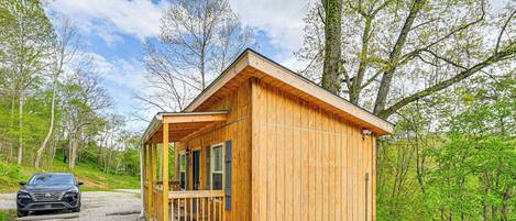 A wooden cabin with a porch, surrounded by trees and a gravel path.